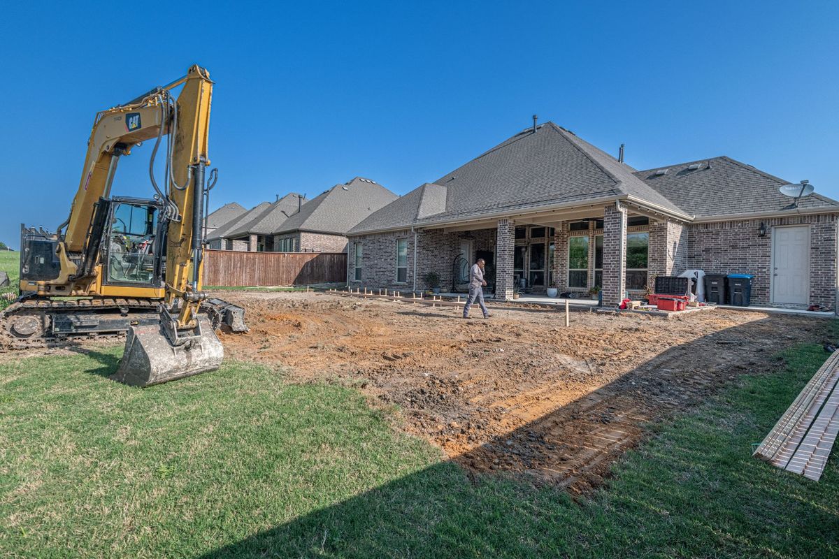 A backyard in Gainesville with a partially installed inground pool excavation, piles of red clay soil beside the hole, construction equipment near a fenced yard, and a finished patio area transitioning into an unfinished pool site to show how site conditions and full project scope affect cost