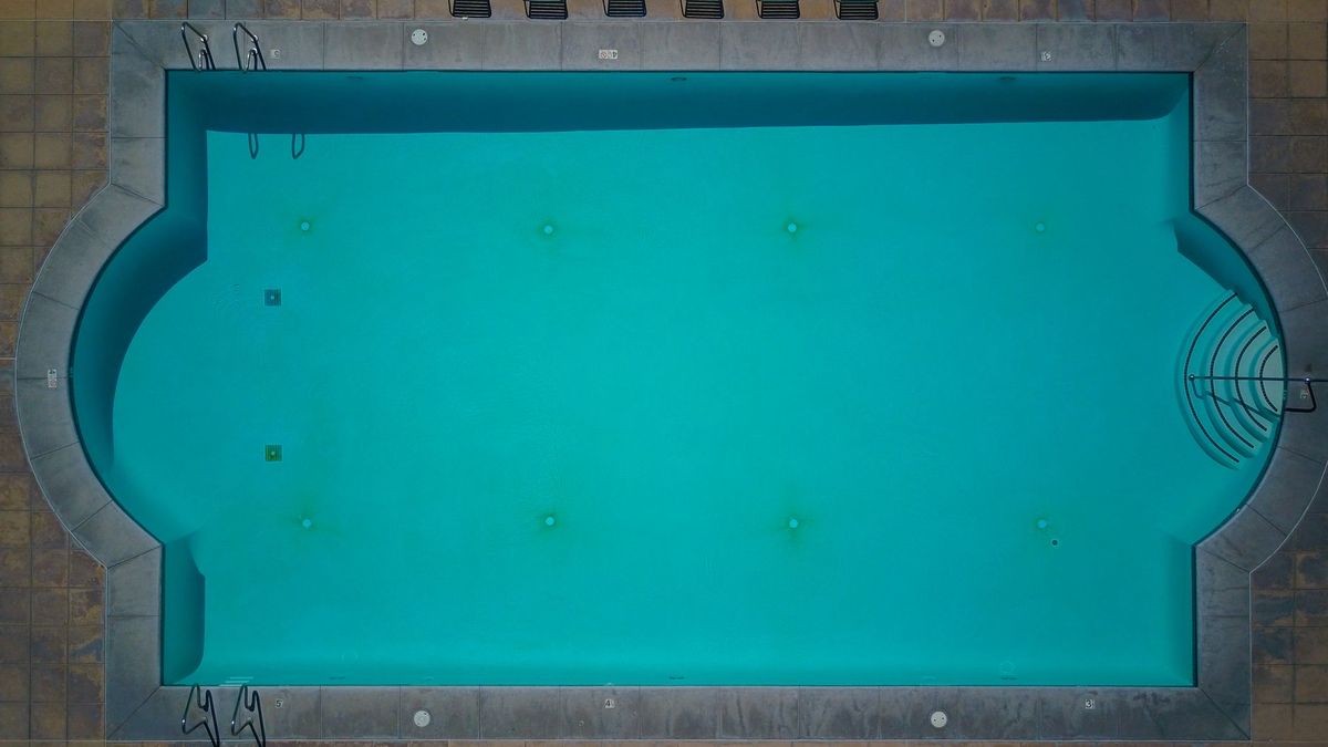 A finished backyard pool equipment area with a variable-speed pump, filter tank, salt chlorinator cell, heater, and control panel mounted on a concrete equipment pad next to a sparkling in-ground pool and a hose being used for water top-off