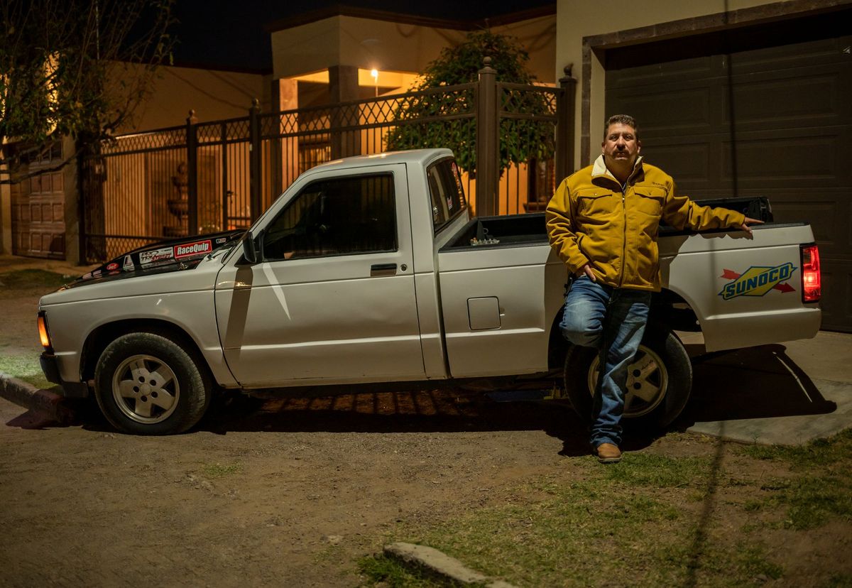 A tense scene at a driveway meeting where one person is pointing at an unfinished contract packet while another gestures impatiently beside a pickup truck, with a handoff envelope, scattered papers, and a half-open backyard gate leading toward a pool construction area